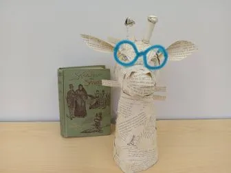 A giraffe head made of book pages with a green book in the background.