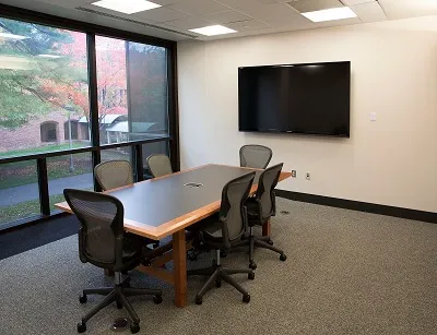 A picture of one of our group study rooms.  It has a table, six chairs, a large TV and floor to ceiling windows looking out over a sidewalk and Palamountian hall.